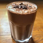 A creamy chocolate banana smoothie in a glass with a straw, featuring rich chocolate tones and banana slices on top.