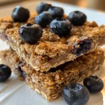 A close-up side view of delicious blueberry oat breakfast bars, showcasing juicy blueberries and a golden brown texture.