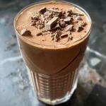 Close-up of a creamy chocolate protein shake in a glass, with a thick texture and optional peanut butter on display.