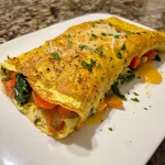 Close-up view of a veggie omelette roll filled with colorful vegetables and cheese.