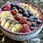 A close-up view of a creamy vanilla berry protein smoothie bowl topped with fresh fruits and granola.