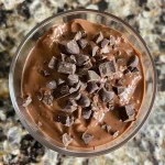 Close-up view of creamy chocolate pudding in a small bowl, topped with a sprinkle of cocoa.