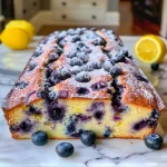 A close-up side view of a moist Blueberry Lemon Loaf with a golden crust and vibrant blueberries.