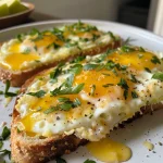 Close-up view of Cheesy Egg Toast with melted cheese and herbs on two slices of toasted bread.