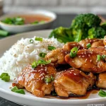 A juicy piece of Teriyaki Chicken glistening with sauce and garnished with sesame seeds and green onions.
