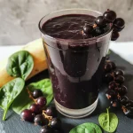 Close-up of a rich, dark purple Black Currants Spinach Smoothie in a clear glass, showcasing its creamy texture.