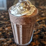 ['A close-up side view of a chocolate chia milkshake in a glass, topped with whipped cream and chia seeds.', 'A decadent chocolate chia milkshake in a tall glass, featuring whipped cream and chia seeds on top.', 'A side view of a creamy chocolate chia milkshake, showcasing its rich color and toppings.', 'A chocolate chia milkshake overflowing with whipped cream and garnished with chia seeds, captured in detail.']