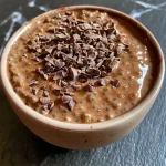 ['Close-up view of a luscious Chocolate Chia Protein Pudding in a clear glass.', 'Side angle of creamy chocolate chia pudding topped with chia seeds.', 'Rich chocolate pudding with chia seeds on a wooden table.', 'Smooth chocolate chia pudding displayed in a stylish glass container.']