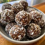 ['Close-up view of shiny Chocolate Coconut Energy Balls on a wooden surface.', 'Delicious Chocolate Coconut Energy Balls, showing a side view with a textured surface.', 'A group of Chocolate Coconut Energy Balls piled together, highlighting their rich chocolate color.', 'Juicy Chocolate Coconut Energy Balls with shredded coconut sprinkled on top, captured in natural light.']