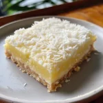 ['A close-up side view of a Coconut Lemon Slice, showcasing its golden crust and moist interior.', 'A beautifully presented slice of Coconut Lemon cake, highlighting the texture and zest of lemon on top.', 'A vibrant Coconut Lemon Slice with a rich lemon glaze, displayed on a white plate.', 'A tantalizing view of a Coconut Lemon Slice, featuring shredded coconut flakes and lemon zest.']