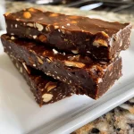 ['Close-up side view of dark chocolate almond energy bars stacked on a wooden surface.', 'Juicy dark chocolate almond energy bars with visible almond chunks and chocolate chips.', 'Side view of energy bars showcasing a glossy dark chocolate coating and almond pieces.', 'Textured energy bars made with cocoa powder and dates, highlighted against a neutral background.']