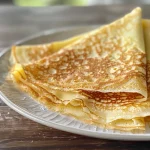 Close-up view of golden gluten-free crepes stacked on a plate.