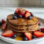 ['Close-up side view of gluten-free vegan strawberry chocolate pancakes topped with fresh strawberries.', 'Juicy gluten-free vegan pancakes layered with strawberries and drizzled with maple syrup.', 'Side view of fluffy vegan pancakes stacked with pieces of strawberries and a dusting of cocoa powder.', 'Delicious-looking gluten-free pancakes presented with sliced strawberries and a rich chocolate color.']