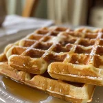 Close-up shot of a golden-brown gluten-free waffle topped with syrup and fresh berries.