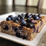 ['Close-up of a slice of blueberry breakfast cake with oatmeal and yogurt, showcasing moist texture.', 'Side view of a healthy yogurt oat blueberry cake, highlighting fresh blueberries on top.', 'Juicy blueberry breakfast cake, featuring a golden crust and dense, moist interior.', 'A delectable slice of breakfast cake filled with blueberries, oats, and yogurt, set on a wooden table.']