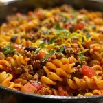['Close-up view of a bowl of One Pot Beef Taco Pasta with melted cheese on top.', 'Side perspective of a colorful One Pot Beef Taco Pasta dish featuring ground beef and vegetables.', 'Juicy One Pot Beef Taco Pasta in a bowl, showcasing its cheesy and flavorful ingredients.', 'Delicious One Pot Beef Taco Pasta with a rich tomato sauce and garnished with peppers and cheese.']