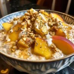 ['Close-up view of a jar of Peaches and Cream Overnight Oats with fresh peach slices on top.', 'Side view of creamy overnight oats topped with chopped peaches and granola in a glass jar.', 'A delicious serving of Peaches and Cream Overnight Oats featuring peach chunks and almond butter.', 'Creamy yogurt-based overnight oats with peaches and a sprinkle of granola, captured in detail.']