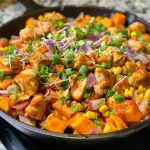 ['A close-up of a savory BBQ chicken sweet potato skillet showing diced sweet potatoes, shredded chicken, and melted cheese.', 'A vibrant skillet filled with BBQ chicken, yellow corn, and sliced red onions on a wooden surface.', 'A side view showcasing juicy BBQ chicken mixed with sweet potatoes, topped with green onions and cheese, served in a skillet.', 'A delicious BBQ chicken sweet potato dish with colorful ingredients photographed from the side, highlighting its textures.']