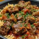 ['A close-up of Beef Giouvetsi featuring tender beef, orzo pasta, and a rich tomato sauce.', 'Side view of a bowl of Beef Giouvetsi, showcasing juicy beef, orzo, and herbs.', 'Detailed image of Beef Giouvetsi with visible ingredients like orzo, beef chunks, and cheese.', 'Close-up shot of a delicious Beef Giouvetsi dish, garnished with parsley and cheese.']