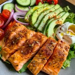 ['A close-up of a creamy salmon salad featuring diced cucumbers, cherry tomatoes, and avocado.', 'Side view of a colorful salmon salad with Greek yogurt dressing garnished with cilantro.', 'Juicy salmon filet atop a salad with vibrant vegetables and a creamy sauce.', 'A delicious bowl of salmon salad showcasing creamy dressing and fresh ingredients.']