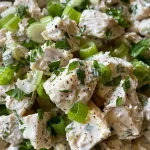['Close-up side view of creamy chicken salad garnished with fresh herbs.', 'Juicy chicken salad with green onions and herbs, viewed from the side.', 'Delicious creamy chicken salad featuring diced celery and herbs in focus.', 'Side angle of a flavorful chicken salad showcasing vibrant green herbs.']