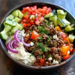 ['A close-up side view of a Greek ground beef bowl topped with tzatziki and fresh vegetables.', 'Juicy Greek ground beef bowl featuring ground beef, tzatziki, and colorful vegetables.', 'Side view of a Greek ground beef bowl with tzatziki, cherry tomatoes, and olives.', 'Close-up of a hearty Greek ground beef bowl garnished with tzatziki and a mix of fresh ingredients.']