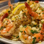 ['A close-up view of juicy shrimp served with lemon rice and a bowl of tzatziki.', 'Side view of a plate featuring Greek shrimp alongside lemon-flavored rice.', 'Detailed shot of succulent shrimp garnished with herbs, accompanied by creamy tzatziki.', 'Close-up image showcasing Greek shrimp and lemon rice plated elegantly with sauce.']