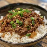 ['Close-up of a bowl filled with ground beef, rice, and garnishes.', 'Side view of a savory Ground Beef Hot Honey Bowl with green onions.', 'Juicy ground beef mixed with rice and hot honey in a vibrant bowl.', 'Delicious bowl featuring ground beef, rice, and sesame seeds.']