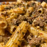 ['Close-up view of juicy pesto beef pasta with vibrant green basil and grated cheese.', 'Side angle of a delicious plate of pesto beef pasta, showcasing pasta texture and toppings.', 'Zoomed-in photo of creamy pesto beef pasta, highlighting the savory ingredients and colorful presentation.', 'Detailed side view of a bowl of pesto beef pasta, featuring fresh herbs and a rich sauce.']