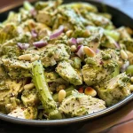 ['Close-up view of a bowl filled with colorful Pesto Chicken Salad, featuring diced chicken and vibrant vegetables.', 'Side view of a delicious Pesto Chicken Salad showcasing bright green pesto and toasted pine nuts.', 'Fresh Pesto Chicken Salad with diced chicken, celery, and red onion, served in a white bowl.', 'Juicy Pesto Chicken Salad close-up, highlighting the creamy texture and vibrant ingredients.']
