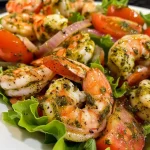 ['A vibrant close-up of a Pesto Shrimp Tomato Salad featuring shrimp, cherry tomatoes, and greens.', 'A colorful side view of a delicious shrimp salad with pesto dressing and chunks of tomato.', 'Detailed image showcasing a fresh salad with shrimp, pesto, and chopped vegetables.', 'A close-up shot of a delectable salad with shrimp, cherry tomatoes, and a drizzle of pesto.']