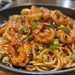 ['A close-up view of Shrimp Teriyaki Pasta featuring large shrimp and colorful toppings.', 'Juicy shrimp atop a bed of soba noodles glazed in teriyaki sauce with scallions.', 'Side view of a bowl filled with Shrimp Teriyaki Pasta garnished with sesame seeds.', 'A mouthwatering presentation of Shrimp Teriyaki Pasta showing vibrant ingredients.']