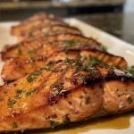 ['Close-up side view of zesty grilled honey mustard salmon on a plate.', 'Juicy grilled salmon fillet coated in honey mustard glaze, garnished with herbs.', 'Side view of a perfectly grilled honey mustard salmon, highlighting its glistening texture.', 'Delicious piece of salmon with a zesty mustard glaze, freshly cooked and garnished.']