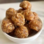 ['Close-up view of Apple Cinnamon Cookie Energy Bites, showcasing their chewy texture and bits of apple.', 'Side view of homemade Apple Cinnamon Cookie Energy Bites with visible oats and cinnamon.', 'Detailed shot of energy bites featuring grated apple and a sprinkle of cinnamon.', 'Close-up image of golden-brown Apple Cinnamon Cookie Energy Bites, highlighting their delicious ingredients.']