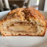 ['Close-up view of a loaf of apple cinnamon sourdough bread with a golden crust.', 'Side view of a freshly baked apple cinnamon sourdough bread showcasing its soft interior and chunks of apple.', 'Textured crust of apple cinnamon sourdough bread with visible pieces of apple and spices.', 'Juicy apple cinnamon sourdough bread displaying a rich brown crust and warm, fluffy interior.']