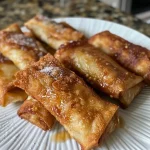 ['Close-up view of crispy apple pie egg rolls stacked on a plate.', 'Side angle of apple pie egg rolls, showcasing their golden-brown texture.', 'A plate of apple pie egg rolls drizzled with caramel sauce, highlighting the filling.', 'Juicy apple pie egg rolls, freshly fried, with a side of whipped cream.']