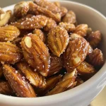 ['Close-up view of golden-brown candied almonds coated in cinnamon and sugar.', 'Side angle of shiny, caramelized almonds sprinkled with cinnamon sugar.', 'Crispy candied almonds displayed in a vibrant bowl, showcasing their glistening surface.', 'A detailed shot of sweet candied almonds, highlighting their irresistible glaze.']