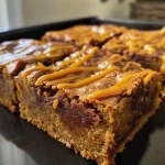 ['Close-up view of golden caramel pumpkin blondies with a drizzle of caramel sauce.', 'Side view of moist pumpkin blondies topped with caramel chips and caramel drizzle.', 'Delicious blondies featuring pumpkin puree and caramel sauce, displayed on a rustic surface.', 'Juicy dessert bars made with pumpkin and caramel, showcasing their rich texture.']