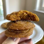 ['Close-up side view of a freshly baked Chai Spiced Pumpkin Cookie with visible spices.', 'Side view of a soft, orange pumpkin cookie topped with a sprinkle of cinnamon.', 'Juicy Chai Spiced Pumpkin Cookie displayed on a wooden surface, showcasing its texture.', 'Warm, spiced pumpkin cookie with a golden-brown exterior, highlighting its moist interior.']