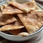 ['A close-up view of crispy cinnamon sugar pita chips arranged on a plate.', 'Side view of golden brown cinnamon sugar pita chips sprinkled with cinnamon and sugar.', 'Juicy cinnamon sugar pita chips with a shiny buttery coating, captured in detail.', 'A close-up shot showcasing the texture of cinnamon sugar pita chips on a wooden table.']