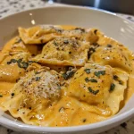 ['Close-up view of creamy pumpkin ravioli topped with Parmesan cheese and herbs.', 'Side angle shot of delicious pumpkin ravioli garnished with nuts and fresh sage.', 'Detailed image showcasing stuffed pumpkin ravioli in a creamy sauce with herbs.', 'Close-up of ravioli with a rich pumpkin filling, drizzled with heavy cream.']