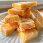 ['Close-up side view of colorful Easy Candy Corn Fudge with yellow and orange layers.', 'Deliciously layered Easy Candy Corn Fudge in vibrant white, yellow, and orange hues.', 'A slice of Easy Candy Corn Fudge showcasing its creamy texture and festive colors.', 'Side view of creamy Easy Candy Corn Fudge, featuring bright yellow and orange stripes.']