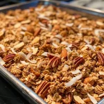 ['Close-up view of crunchy granola clusters with nuts and coconut.', 'Textured granola made from oats, almonds, and pecans displayed on a dark surface.', 'Delicious homemade granola clusters featuring oats, coconut, and sunflower seeds.', 'Appealing clusters of granola with a mix of nuts and coconut flakes.']