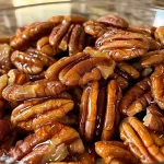 ['Close-up view of shiny honey roasted pecans with a rich caramel glaze.', 'Side profile of honey roasted pecans showcasing their glossy texture and warmth.', 'Detailed image of pecan halves coated in honey, highlighting their golden brown color.', 'Visually appealing shot of crunchy honey roasted pecans arranged attractively.']