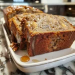 ['A close-up side view of a loaf of Maple Banana Bread with a golden crust and visible walnut chunks.', 'A mouthwatering slice of Maple Banana Bread displaying a moist texture and topped with drizzled maple syrup.', 'A detailed view of Maple Banana Bread with a soft crumb, showcasing its banana pieces and a glossy maple glaze.', 'A beautifully baked loaf of Maple Banana Bread, highlighting the rich colors and nutty toppings.']
