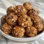['Close-up view of No Bake Pumpkin Spice Energy Bites with a textured surface and chocolate chips.', 'Delicious No Bake Pumpkin Spice Energy Bites stacked on a white plate, showcasing their creamy texture.', 'A side view of No Bake Pumpkin Spice Energy Bites, highlighting the colorful ingredients within.', 'Hand holding a No Bake Pumpkin Spice Energy Bite, with a blurred background of a kitchen setting.']