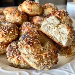 ['Close-up view of golden brown High-Protein Bagel Bites arranged on a wooden board.', 'Side view of freshly baked High-Protein Bagel Bites with a creamy texture visible.', 'Juicy High-Protein Bagel Bites topped with Everything But The Bagel seasoning on a plate.', 'Appetizing High-Protein Bagel Bites showcasing a soft interior and crispy exterior.']
