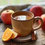 ['A close-up side view of a steaming cup of hot spiced apple cider with cinnamon sticks.', 'A warm bowl of hot spiced apple cider filled with apple slices and orange, garnished with spices.', 'A vibrant cup of hot spiced apple cider surrounded by fresh apples and spices, steaming gently.', 'A detailed view of hot spiced apple cider, showing orange slices and aromatic spices in a clear mug.']
