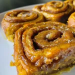 ['Close-up view of a moist vegan pumpkin cinnamon roll topped with glaze.', 'Side view of a stack of vegan pumpkin cinnamon rolls drizzled in frosting.', 'Delicious vegan pumpkin cinnamon rolls with a soft, fluffy texture.', 'Glazed vegan pumpkin cinnamon roll with visible pumpkin and cinnamon swirls.']