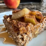 Close-up view of a bowl of baked oats topped with apple slices and cinnamon.